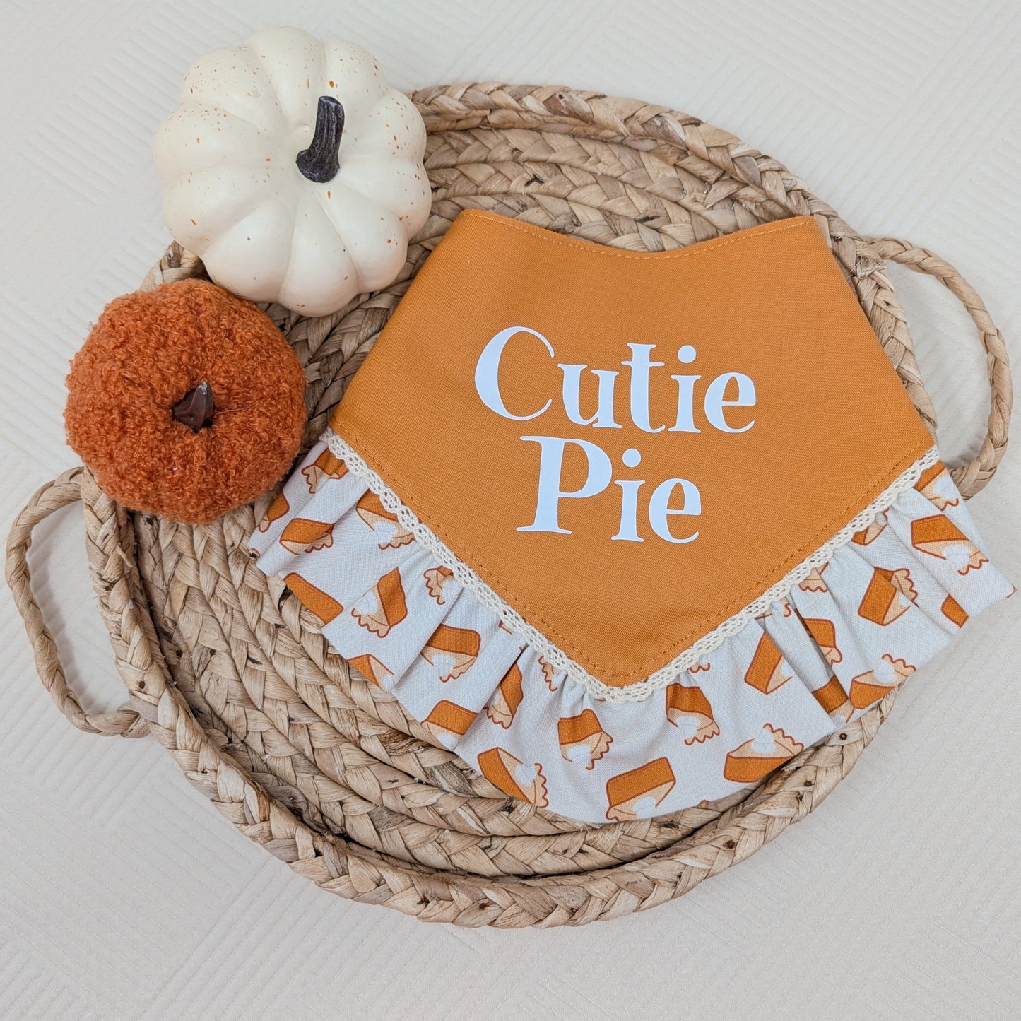 Orange  dog bandana with 'Cutie Pie' text on a woven basket with pumpkins