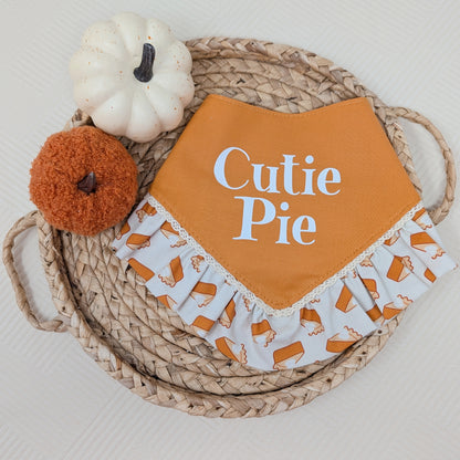 Orange  dog bandana with 'Cutie Pie' text on a woven basket with pumpkins
