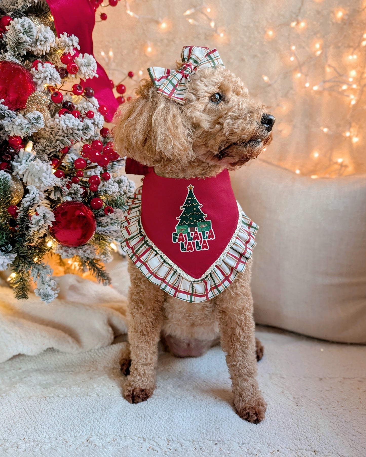 Dog wearing a festive red harness with a Christmas tree design, standing in front of a decorated Christmas tree.
