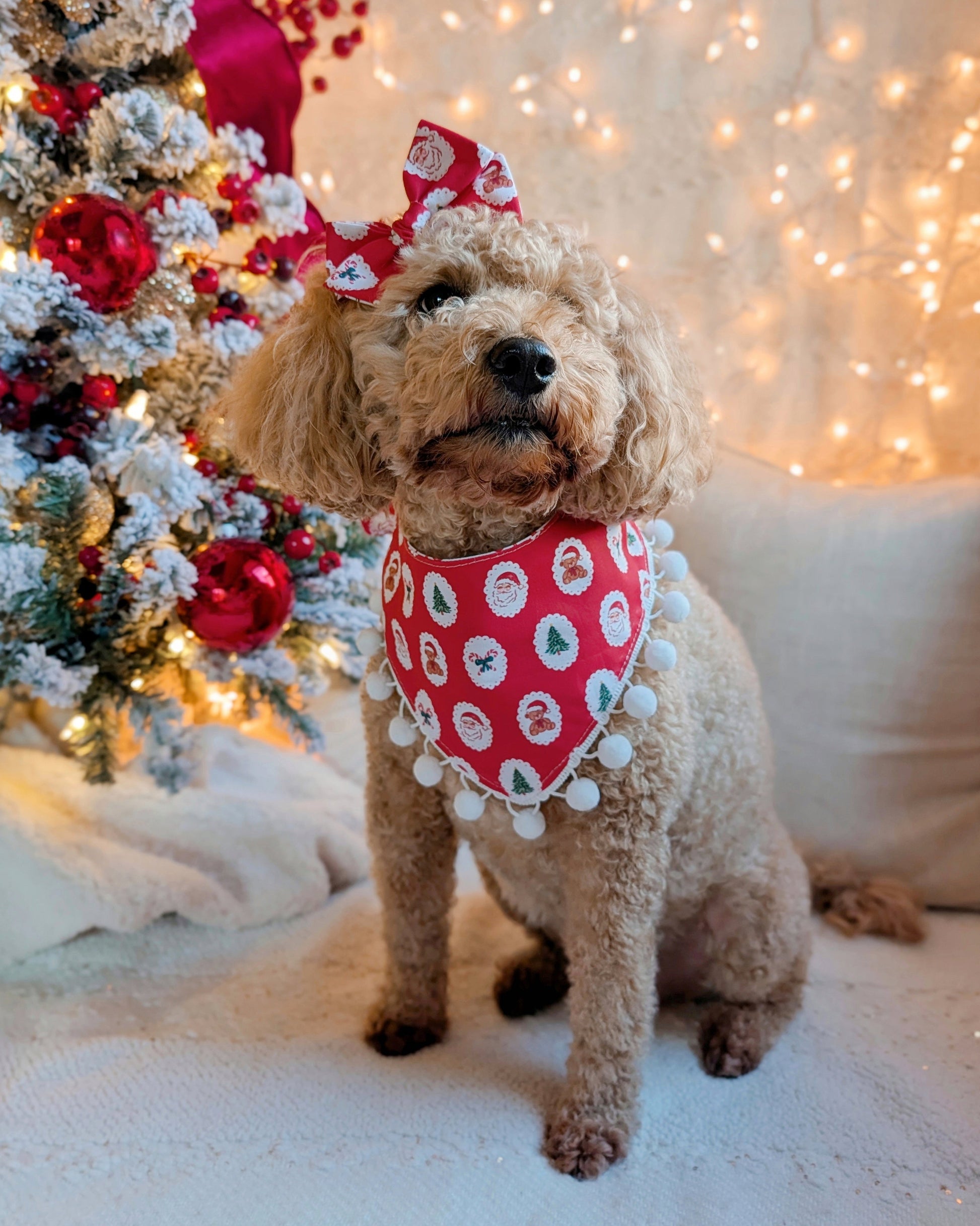Dog wearing a festive bandana  in front of a decorated Christmas tree.